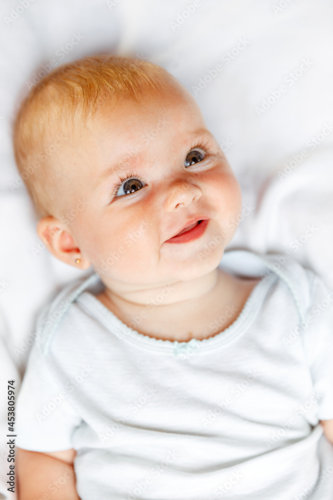 Cute little newborn girl with smiling face looking at camera on white background. Infant baby resting playing lying down on crib bed at home. Motherhood happy child concept Cute little newborn girl with smiling face looking at camera on white background. Infant baby resting playing lying down on crib bed at home. Motherhood happy child concept