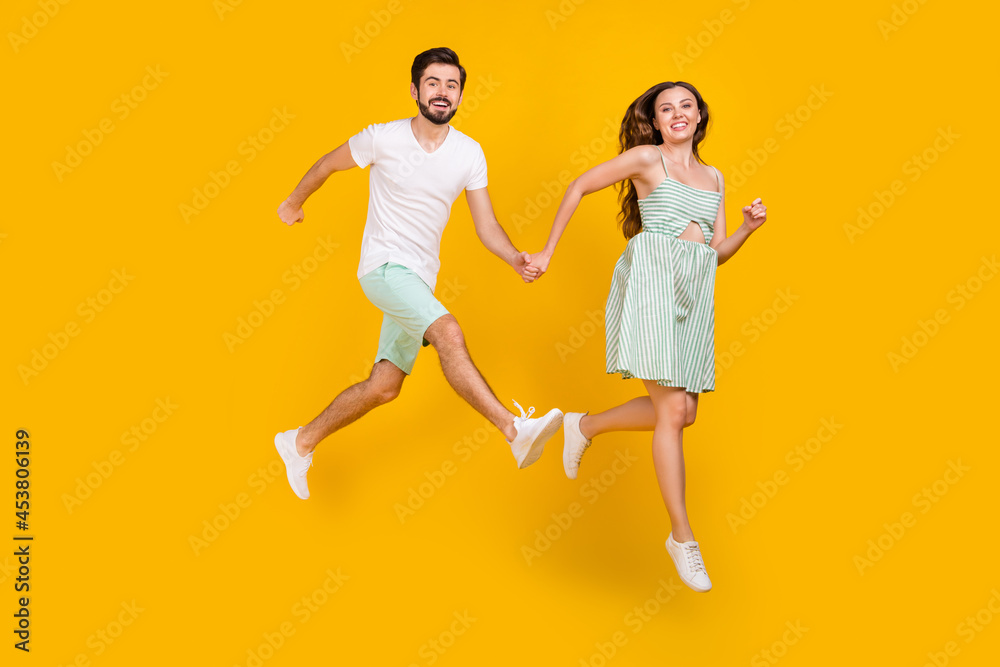Photo of crazy active couple jump hold hands enjoy flight wear casual outfit isolated yellow color background