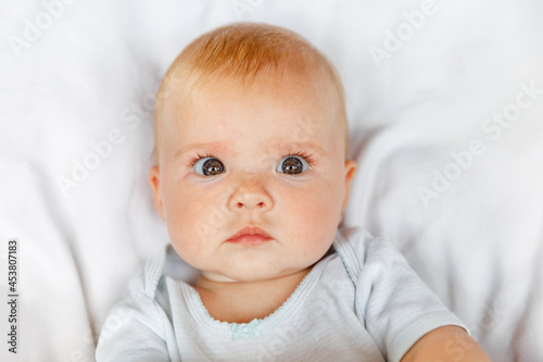 Cute little newborn girl with funny face looking at camera on white background. Infant baby resting playing lying down on crib bed at home. Motherhood happy child concept