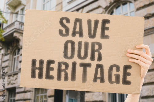 The phrase " Save our heritage " on a banner in men's hand with blurred background. Antiquity. Renovation. Architecture. City. Urban. Real estate. Protest