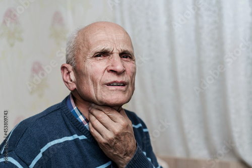 Old pensioner man holding throat with hand and has face with pain grimace. photo