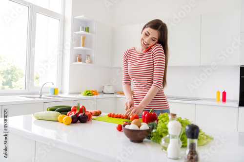 Photo of pretty young cheerful happy woman hold phone talk knife make salad indoors inside house home kitchen