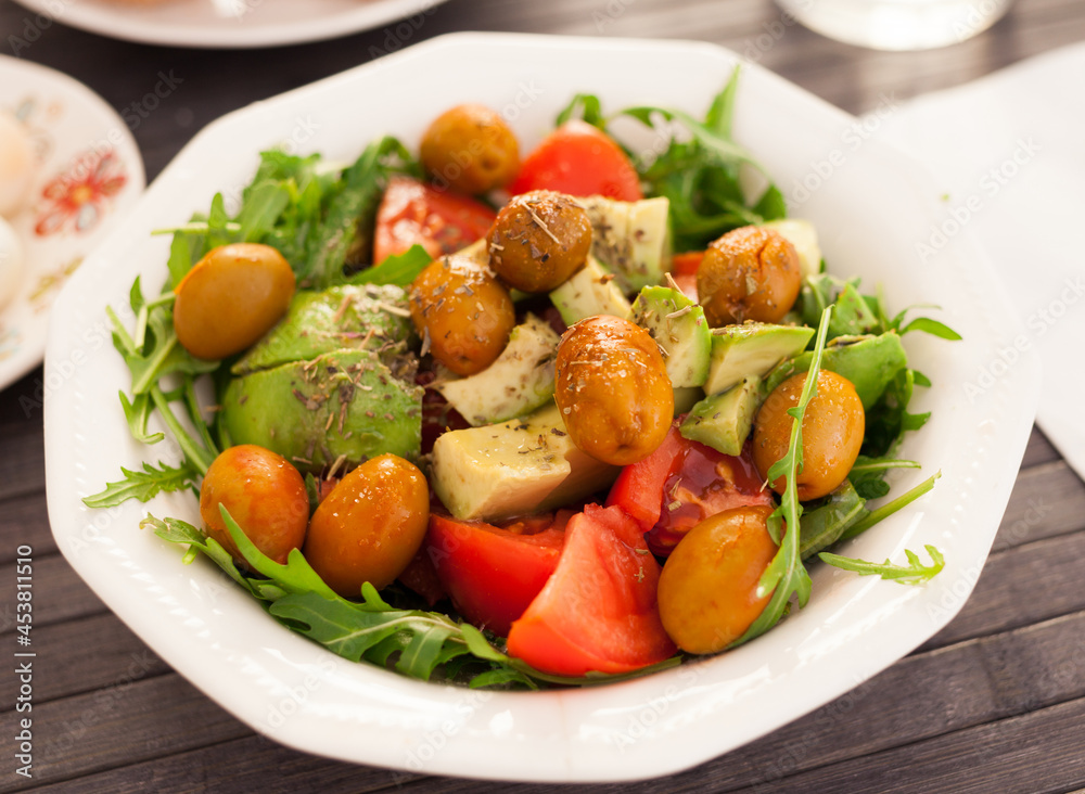 dish of fresh vegetables arugula, avocado, cherry tomatoes with olives on dining table