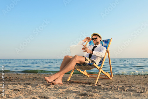 Canvas Print Happy man with laptop resting on deckchair near sea
