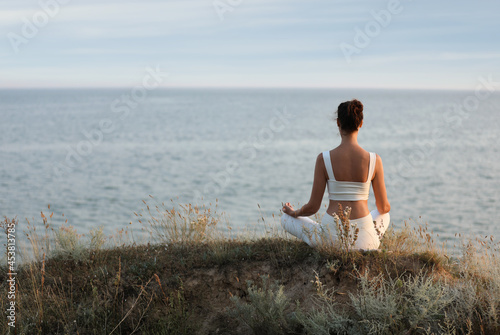 Woman meditating near sea, back view. Space for text