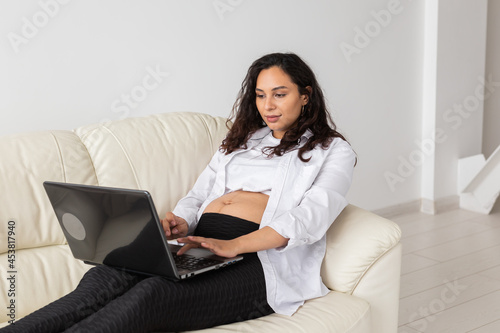 Pregnant woman using laptop while sitting on a couch in the living room at home