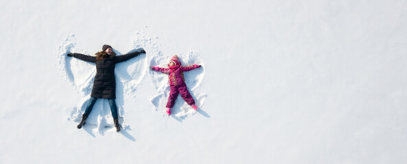 Child girl and mother playing and making a snow angel in the snow. Top flat overhead view