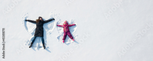 Child girl and mother playing and making a snow angel in the snow. Top flat overhead view photo