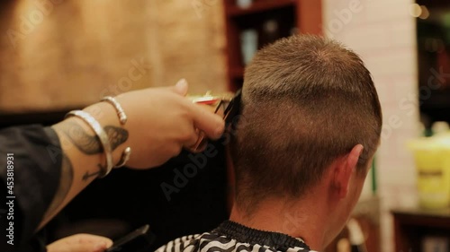 Close-up of the hands of a barber with a tattooed arm cutting a young boy's hair photo