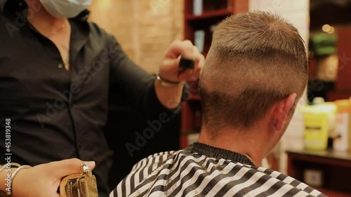 Close-up of the hands of a barber with a tattooed arm cutting a young boy's hair photo