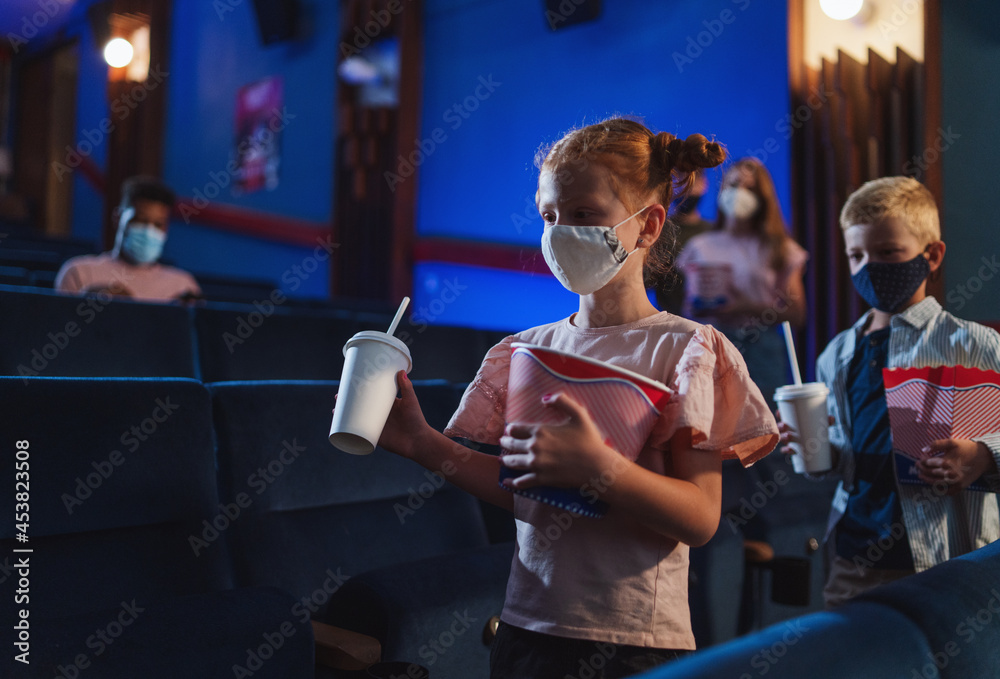 Happy small children with popcorn walking in the cinema, coronavirus concept.
