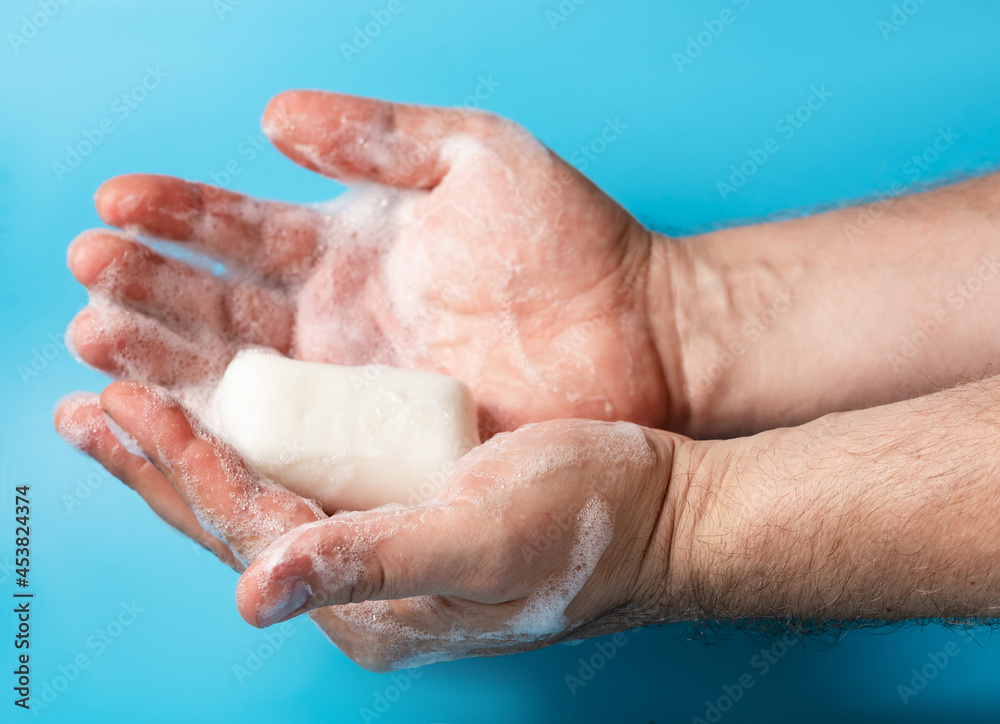 Global Handwashing Day, personal hygiene concept. A man's hand in foam holds soap on a blue background. Global Handwashing Day, personal hygiene concept. A man's hand in foam holds soap on a blue background.