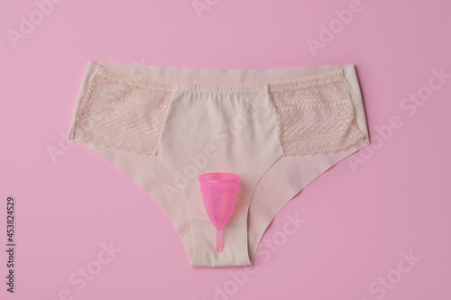 Panties and menstrual cup on pink background, top view