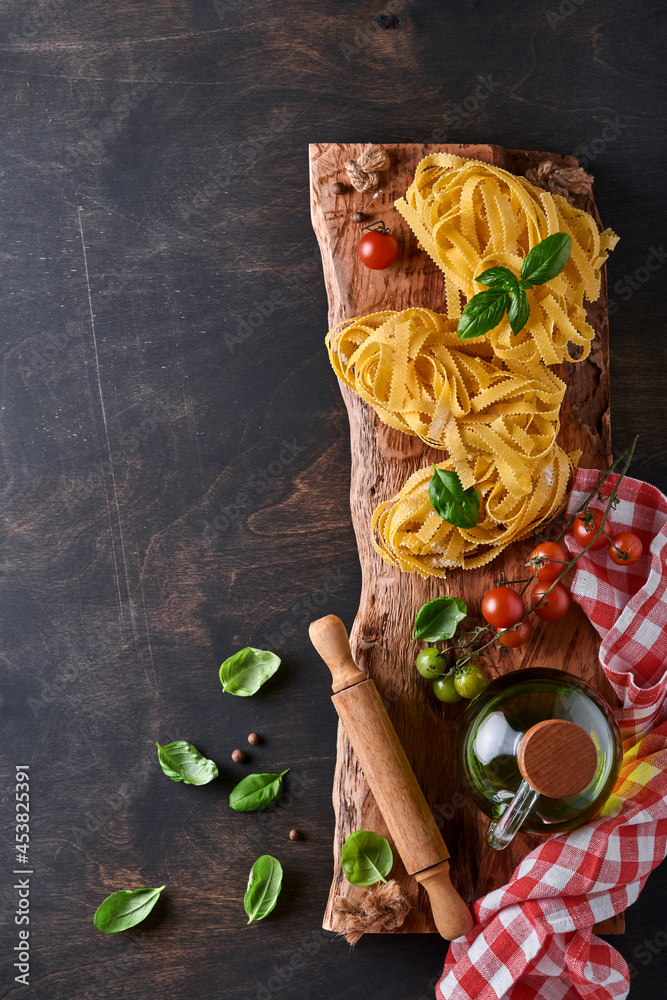 Tagliatelle. Homemade pasta, basil leaves, flour, pepper, olive oil, cherry tomato and rolling pin and pasta knife on dark old wooden background. Food concept. Mock up. Horizontal with copy space.
