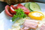 Fried eggs with pieces of bacon, tomatoes and cucumbers. Breakfast on a white plate