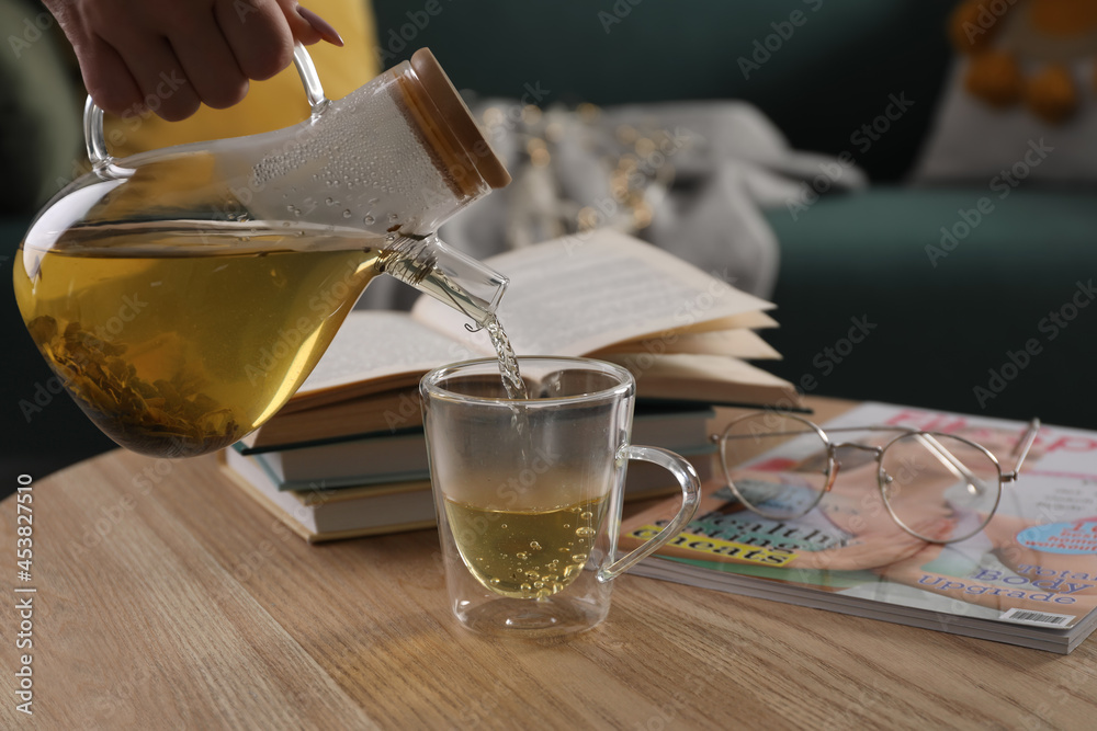 Woman pouring freshly brewed tea into cup at table in living room, closeup. Cozy home atmosphere Woman pouring freshly brewed tea into cup at table in living room, closeup. Cozy home atmosphere