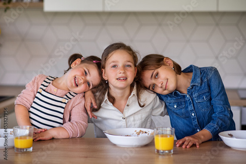 Portrait of three girls sisters indoors at home  looking at camera when eating breakfast.