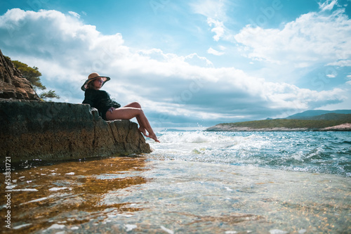Amazing view of a brunette sitting on a rock near the sea. Amazing summer weather in Croatia , vis island. Sunbathing in the sun with waves hitting the shore