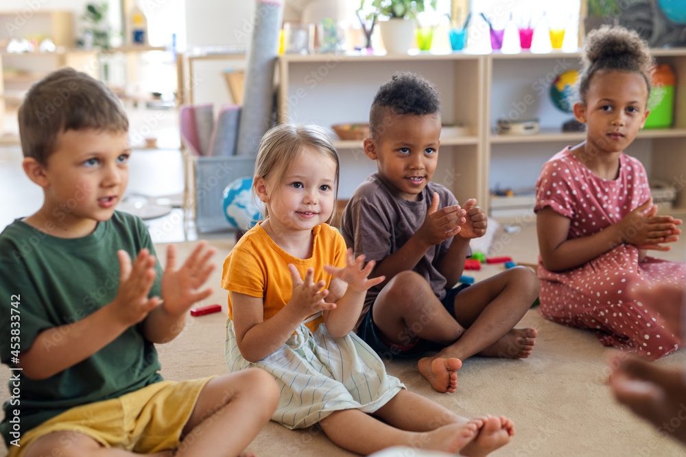 Group of small nursery school children sitting on floor indoors in classroom, clapping. Group of small nursery school children sitting on floor indoors in classroom, clapping.