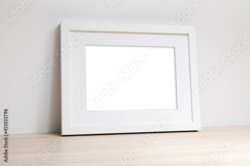 Pusta biała rama na zdjęcia na komodzie oparta o ścianę