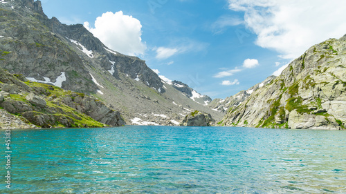 Mountain lake in Aosta Valley, Italy, named "Bellacomba Lake", during springtime. Turquoise waters on the foreground. Rock slopes with snow patches. Blue sky with clouds on the background.