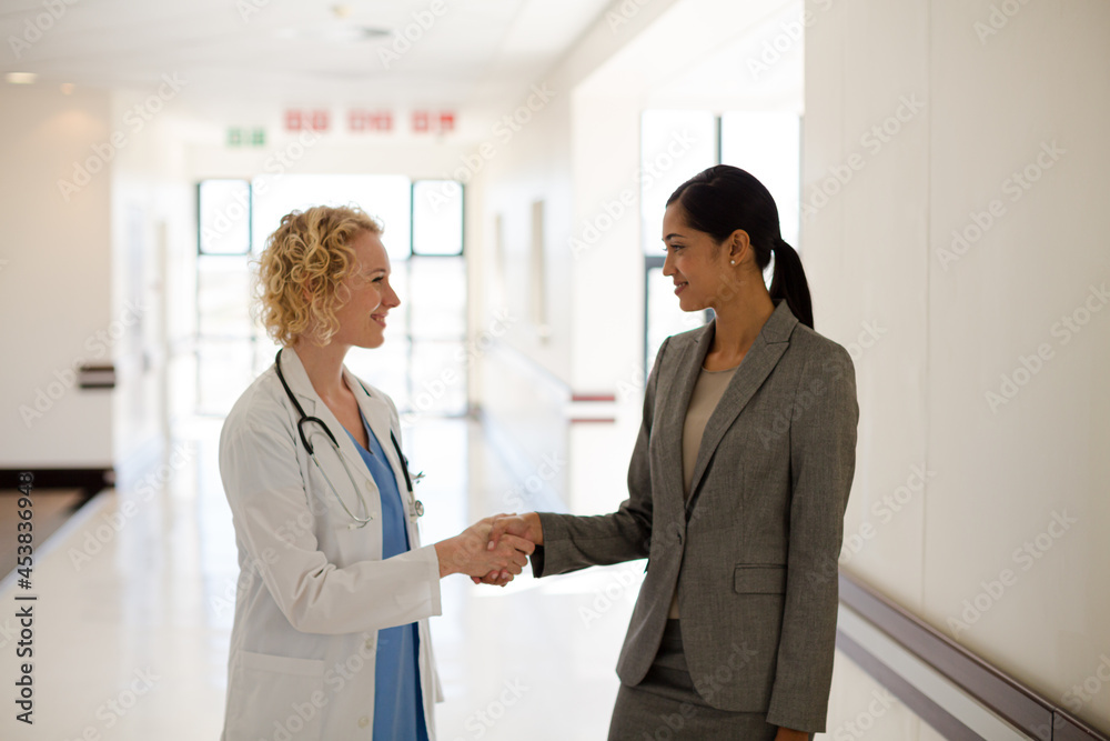 Doctor and businesswoman handshaking in hospital corridor Doctor and businesswoman handshaking in hospital corridor