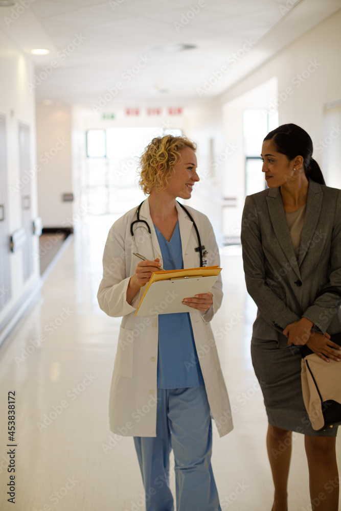 Doctor and businesswoman walking in hospital corridor Doctor and businesswoman walking in hospital corridor