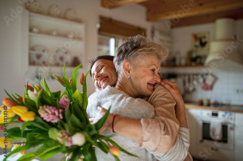 Happy senior mother hugging adult daughter indoors at home, mothers day or birthday celebration. photo