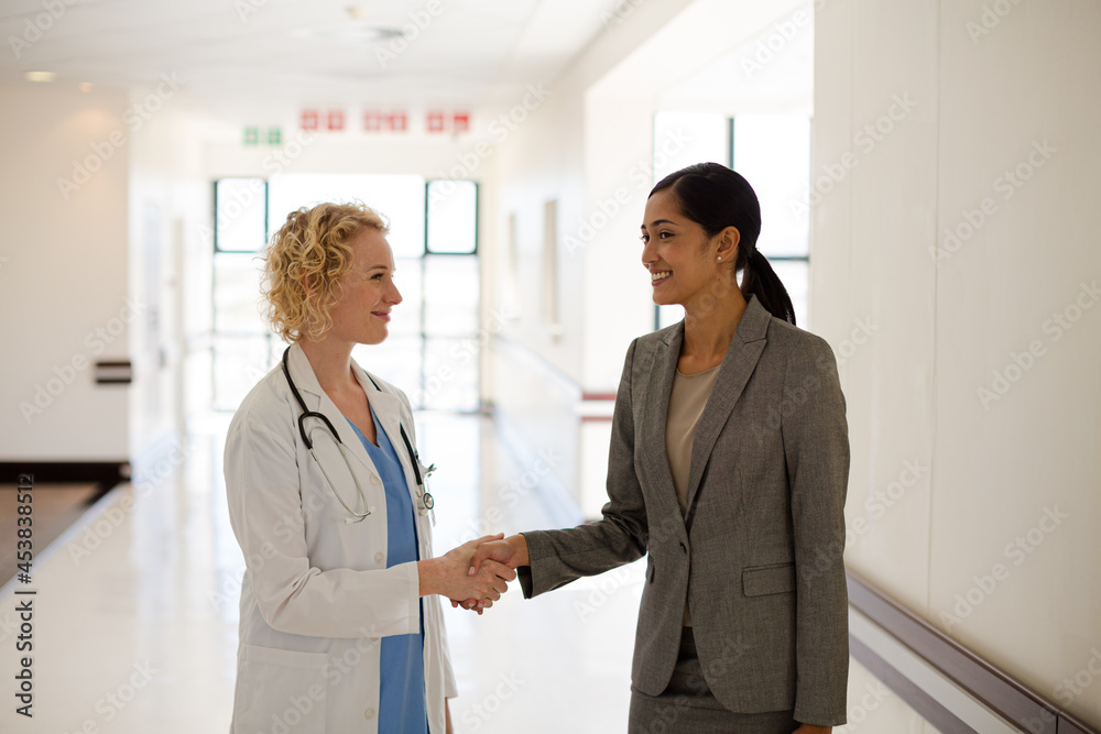 Doctor and businesswoman handshaking in hospital corridor