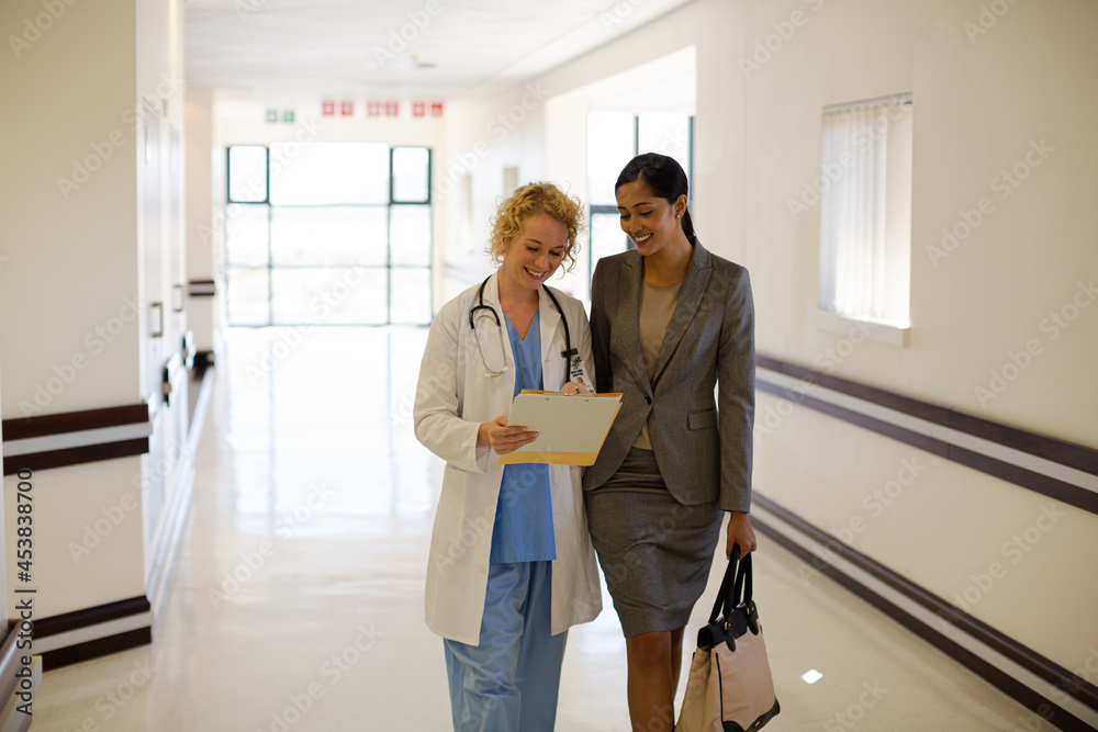 Doctor and businesswoman walking in hospital corridor Doctor and businesswoman walking in hospital corridor