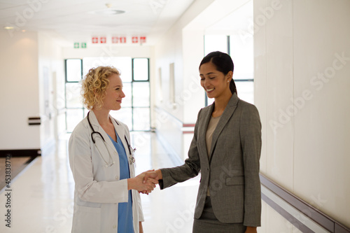 Doctor and businesswoman handshaking in hospital corridor