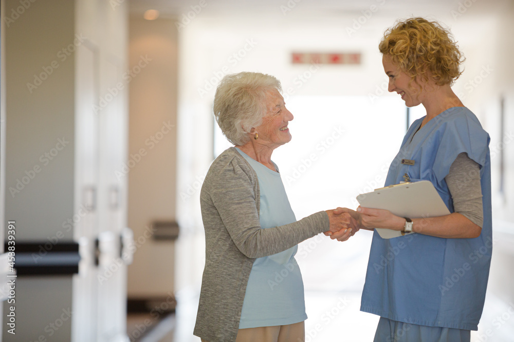 Fototapeta premium Nurse and senior patient shaking hands in hospital corridor