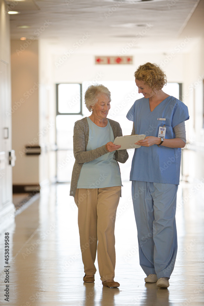 Fototapeta premium Nurse and aging patient reading chart in hospital corridor