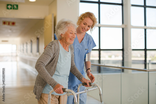 Nurse helping senior patient with walker in hospital corridor