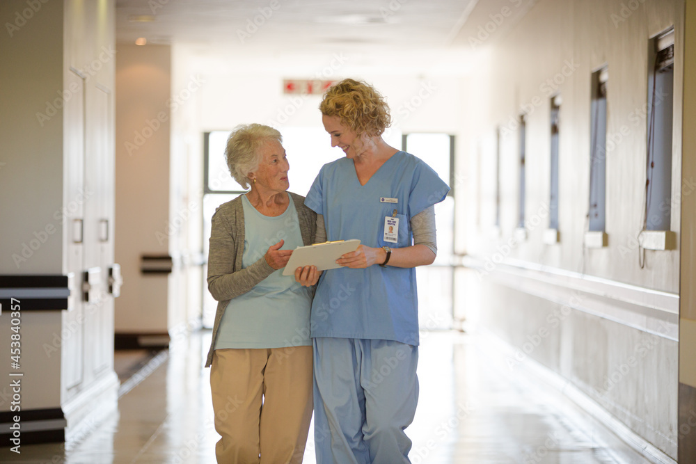Obraz premium Nurse and aging patient reading chart in hospital corridor