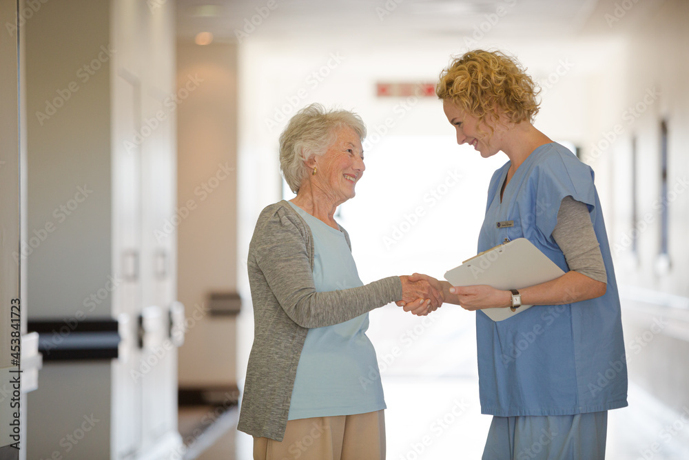 Fototapeta premium Nurse and senior patient shaking hands in hospital corridor