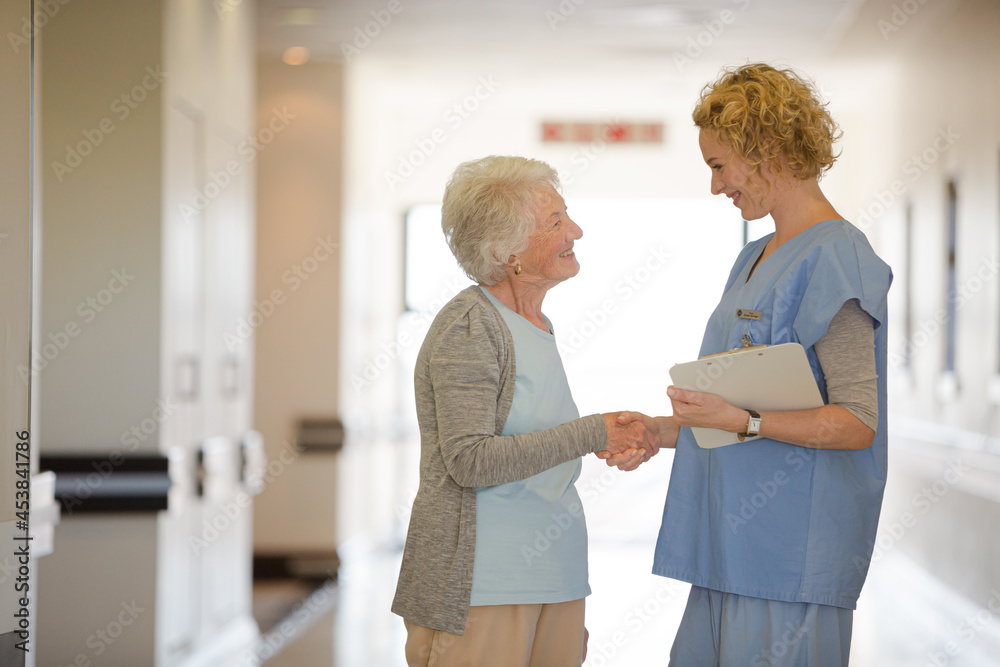 Fototapeta premium Nurse and senior patient shaking hands in hospital corridor