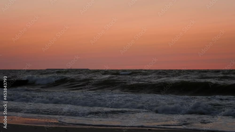Picturesque view of waves of sea in motion of running against sunset sky. Underexposed video clip of oceans waves rolling towards the beach after a vibrant sunset. Picturesque view of waves of sea in motion of running against sunset sky. Underexposed video clip of oceans waves rolling towards the beach after a vibrant sunset.