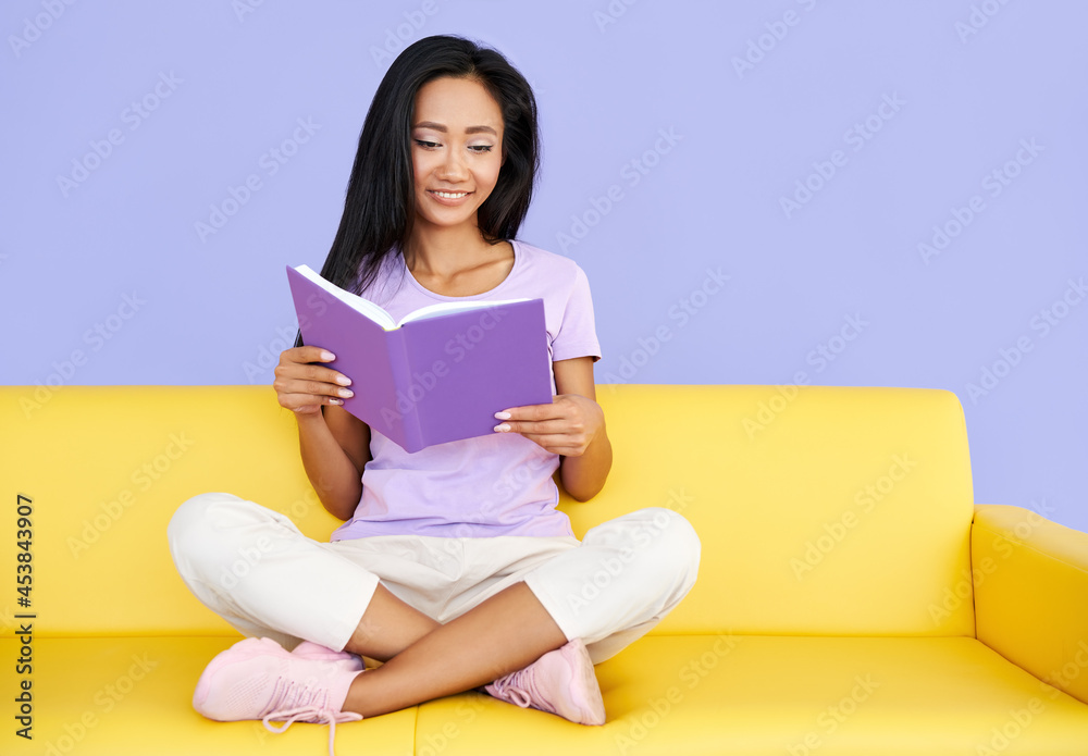 Pretty asian woman reading book sitting at cozy yellow couch, concepts of home and comfort Pretty asian woman reading book sitting at cozy yellow couch, concepts of home and comfort