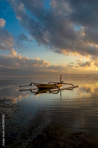 Fishing boat at sunrise Bali coral beach, on the seascape background