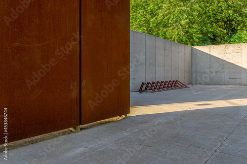 Wall made of architectural concrete and corten sheet surrounded by greenery in the park, a bicycle rack standing on a concrete floor