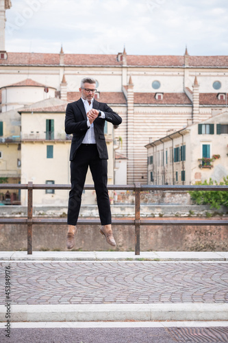 Handsome businessman checking the time on his watch and jumping from stationary. Strange and surreal situation © damianobuffo