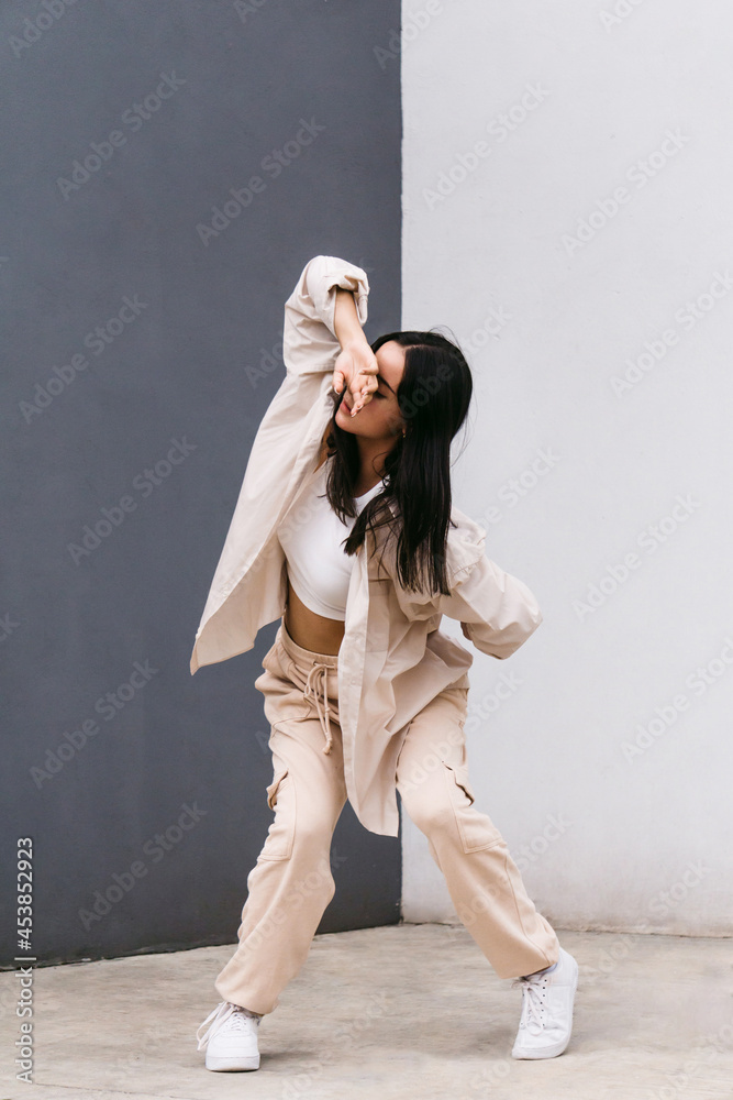 Flexible woman dancing near grey and white wall in city Flexible woman dancing near grey and white wall in city