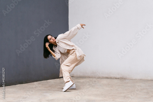 Flexible woman dancing near grey and white wall in city photo