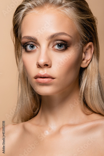 blonde woman with grey eyes and perfect skin looking at camera isolated on beige