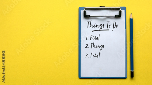Φωτογραφία Top view of a pencil and a clipboard with paper written with Things To Do and a number with sentence First Things First on a yellow background with copy space