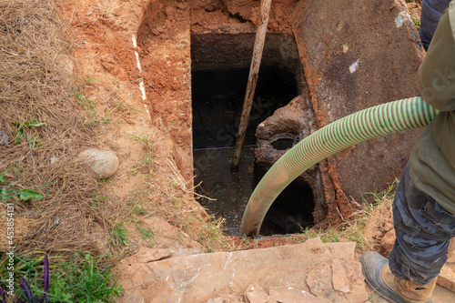 Man holding a pipe as he pumps a septic tank full of sludge, horizontal aspect