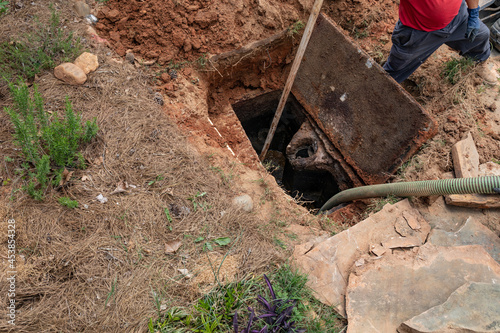 Man using a very long handled shovel to loosen septic sludge as tank is being pumped, horizontal aspect