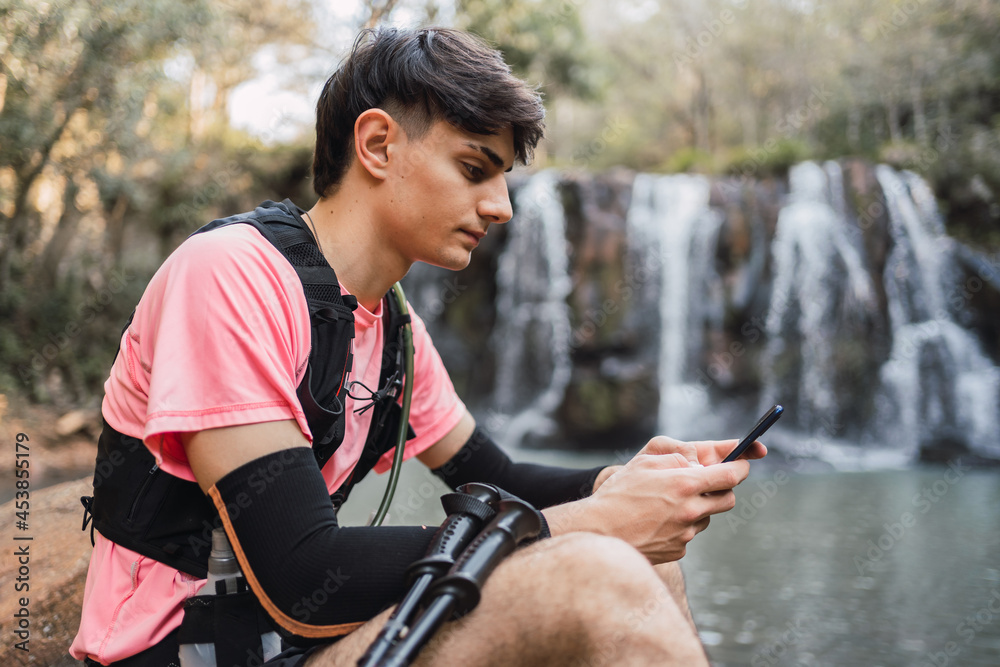 Traveling man drinking from hydration pack near waterfall in woods Traveling man drinking from hydration pack near waterfall in woods