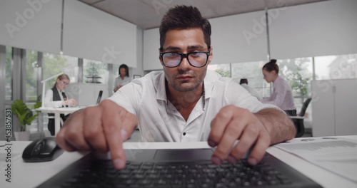 Handsome confident businessman sit down at workplace work on laptop looking at screen